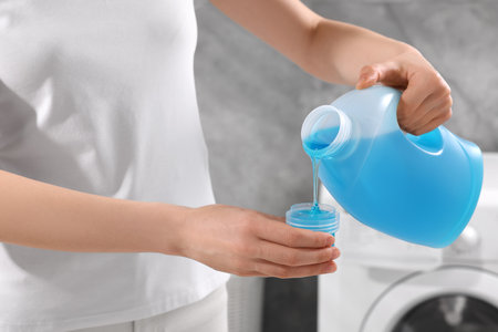 Woman pouring fabric softener from bottle into cap for washing clothes indoors, closeupの写真素材