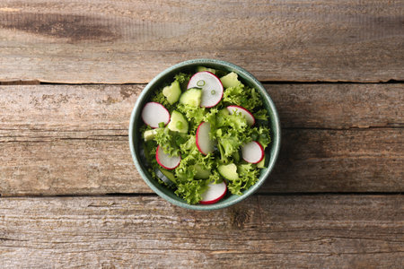 Delicious salad with radish, lettuce and cucumbers in bowl on wooden table, top viewの写真素材