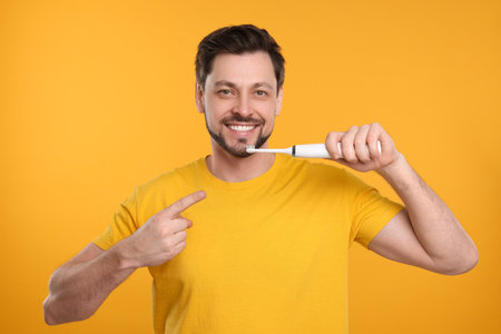 Happy man holding electric toothbrush on yellow backgroundの写真素材