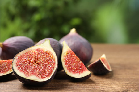 Whole and cut ripe figs on wooden table against blurred green background, closeup. Space for textの写真素材