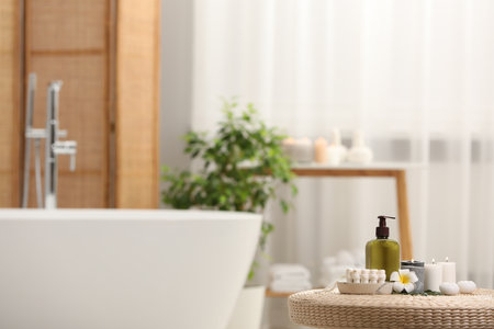 Spa products, burning candles and plumeria flower on wicker table in bathroom. Space for textの写真素材