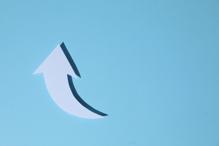 White curved paper arrow on light blue background, top view. Space for textの写真素材
