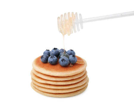 Pouring honey onto delicious pancakes with blueberries on white backgroundの写真素材