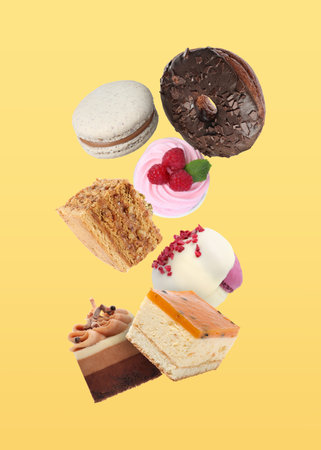 Many different tasty desserts falling on yellow backgroundの写真素材