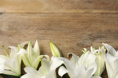 Beautiful white lily flowers on wooden table, flat lay. Space for textの写真素材