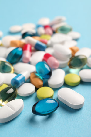 Pile of different pills on light blue background, selective focusの写真素材