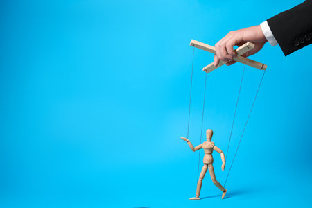 Man pulling strings of puppet on light blue background, closeup. Space for textの写真素材