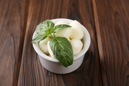 Tasty mozarella balls and basil leaves in bowl on wooden table, closeupの写真素材