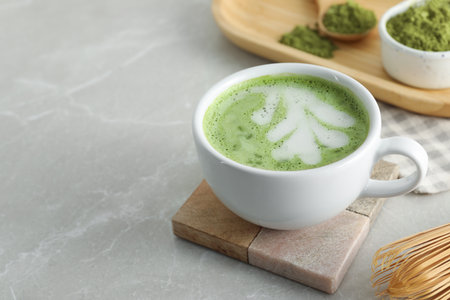 Cup of fresh matcha latte on light gray marble table, closeup. Space for text