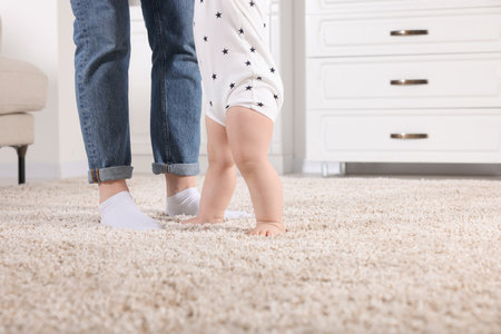 Mother supporting her baby son while he learns to walk on carpet at home, closeup. Space for textの写真素材