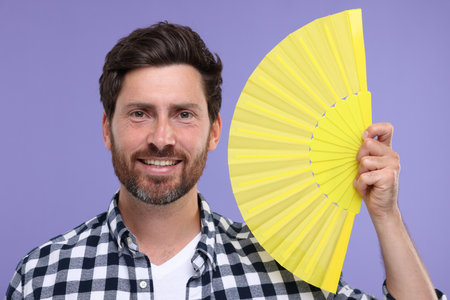 Happy man holding hand fan on purple backgroundの写真素材