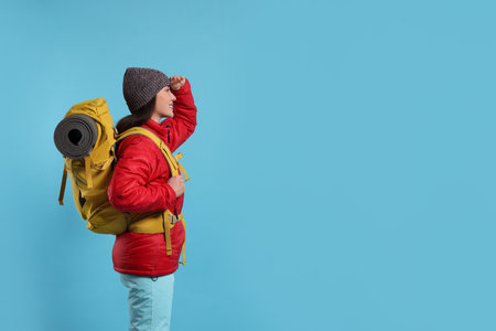 Smiling young woman with backpack on light blue background, space for text. Active tourismの写真素材