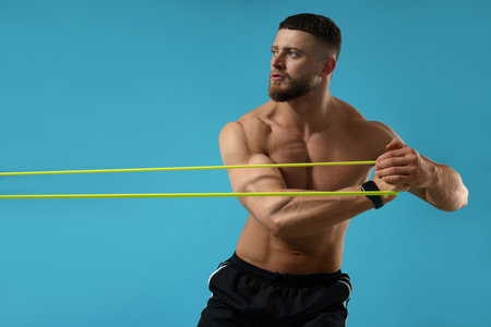 Muscular man exercising with elastic resistance band on light blue backgroundの写真素材