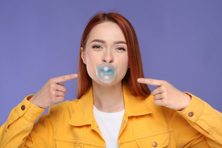 Beautiful woman blowing bubble gum on purple backgroundの写真素材