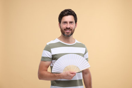 Happy man holding hand fan on beige backgroundの写真素材