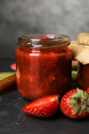 Jar of tasty rhubarb jam and strawberries on dark textured tableの写真素材