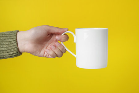 Woman holding white mug on yellow background, closeupの写真素材