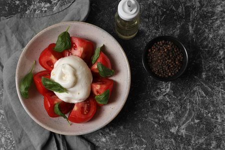 Delicious burrata cheese with tomatoes and basil, oil and peppercorns on gray table, flat lay