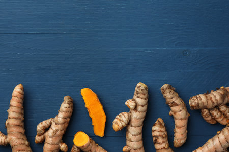 Whole and cut turmeric roots on blue wooden table, flat lay. Space for textの写真素材