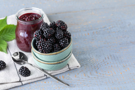 Fresh ripe blackberries and tasty jam on light gray wooden table. Space for textの写真素材
