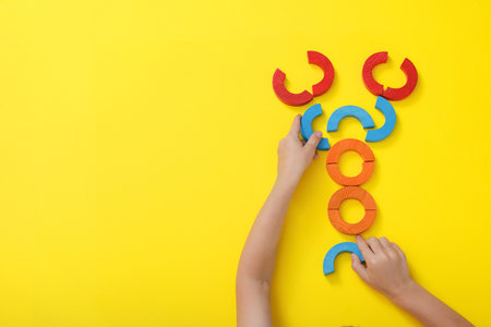 Motor skills development. Boy playing with colorful wooden arcs at yellow table, top view. Space for...