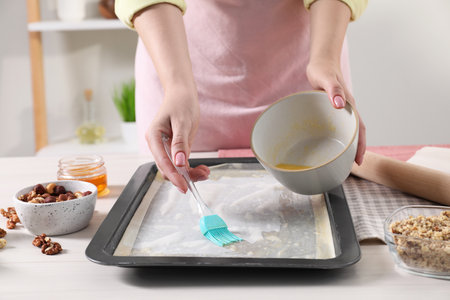 Making delicious baklava. Woman buttering dough in baking pan at white wooden table, closeupの写真素材