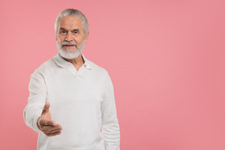 Senior man welcoming and offering handshake on pink background, space for text