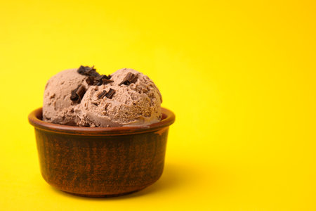 Bowl of tasty ice cream with chocolate chunks on yellow background, closeup. Space for textの写真素材