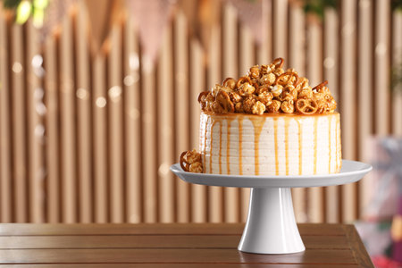 Caramel drip cake decorated with popcorn and pretzels on wooden table, space for textの写真素材
