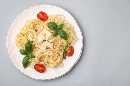 Delicious pasta with brie cheese, tomatoes and basil leaves on gray background, top view. Space for textの写真素材