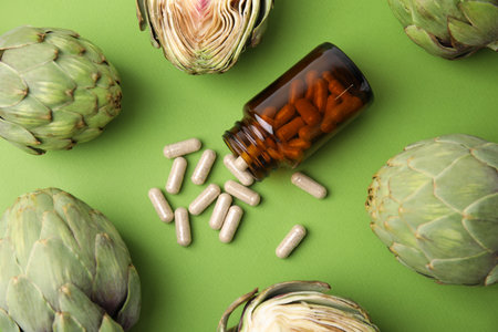 Bottle with pills and fresh artichokes on light green background, flat layの写真素材