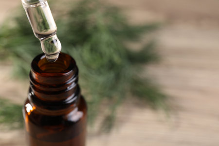 Dripping dill essential oil from pipette into bottle on light background, closeup. Space for textの写真素材