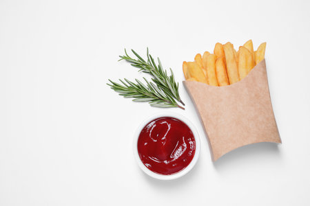 Paper cup with French fries, rosemary and ketchup on white table, flat lay. Space for textの写真素材