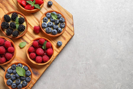 Tartlets with different fresh berries on light gray table, top view and space for text. Delicious dessertの写真素材
