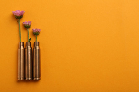 Beautiful flowers in bullet cases on orange background, flat lay. Space for textの写真素材