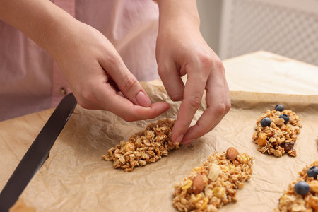 Making granola bars. Woman putting mixture of oat flakes, dry fruits and other ingredients onto baking tray at table in kitchen, closeupの写真素材