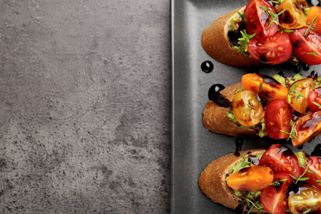 Delicious bruschettas with avocado, tomatoes and balsamic vinegar on gray textured table, top view. Space for textの写真素材