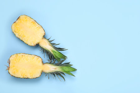 Halves of ripe pineapple on light blue background, flat lay. Space for text