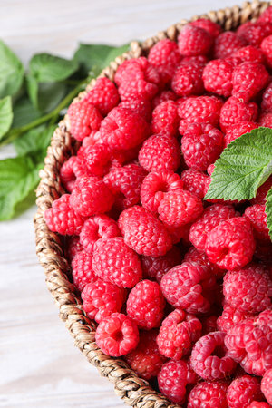 Tasty ripe raspberries in wicker basket on table, closeup