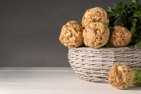 Fresh raw celery roots in wicker basket on white wooden table. Space for text