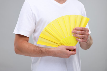 Man holding hand fan on light gray background, closeupの写真素材