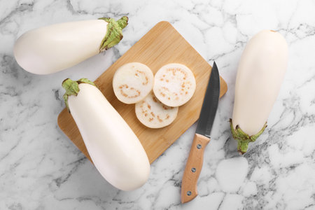 Wooden board, raw white eggplants and knife on marble table, flat layの写真素材