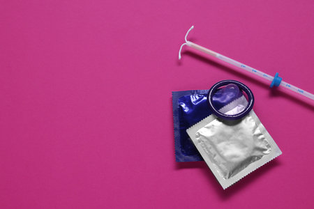 Condoms and intrauterine device on pink background, flat lay and space for text. Choosing...