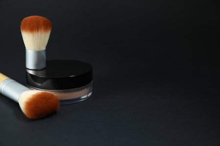 Face powder and makeup brushes on black background, space for textの写真素材
