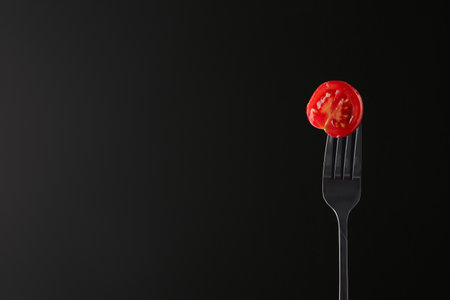 Fork with half of cherry tomato on black backgroundの写真素材