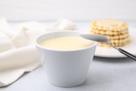 Tasty condensed milk in bowl and spoon on light gray table, closeupの写真素材
