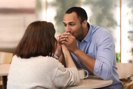 Romantic date. Guy kissing his girlfriend's hands in cafeの写真素材