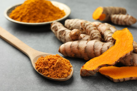 Aromatic turmeric powder and raw roots on gray table, closeupの写真素材