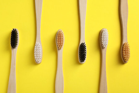 Bamboo toothbrushes on yellow background, flat lay