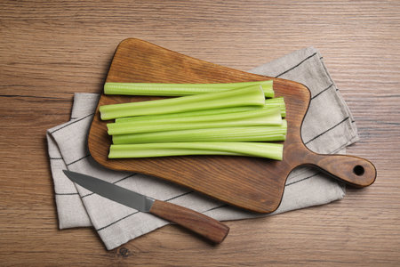 Board with fresh green celery and knife on wooden table, flat layの写真素材